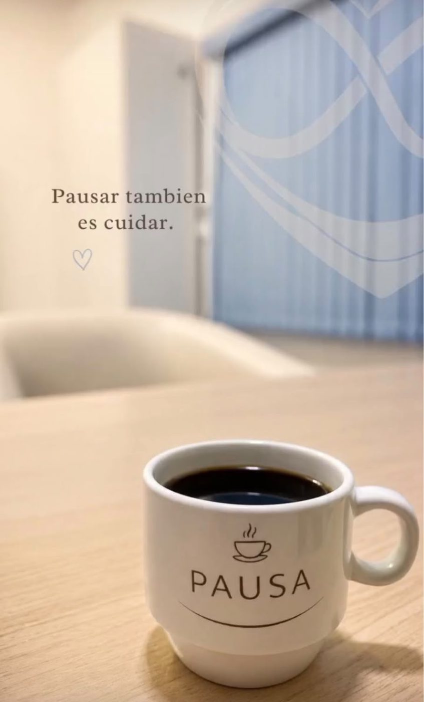 Una taza de café con la palabra Pausa sobre una mesa de la clínica, con el logo en la ventana