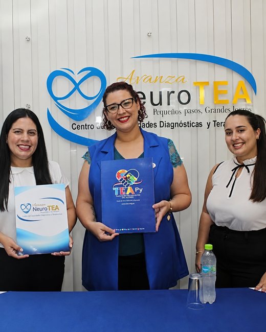 Firma del convenio entre Avanza NeuroTEA y la Asociación TEA Paraguay: tres profesionales sostienen las carpetas de ambas instituciones frente al cartel de la clínica