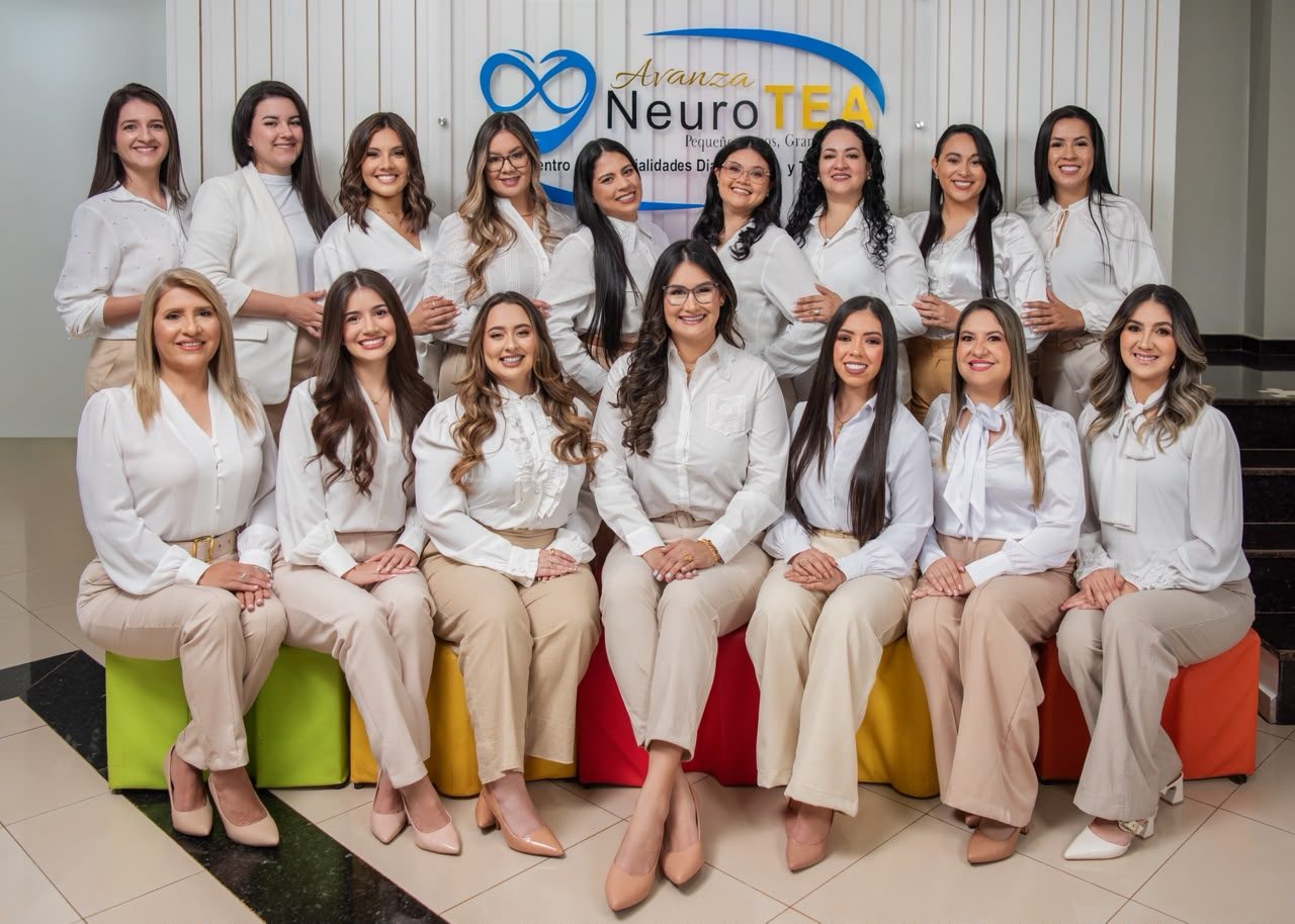 Las dieciséis profesionales del equipo de Avanza NeuroTEA, con uniforme blanco y beige, frente al logo de la clínica