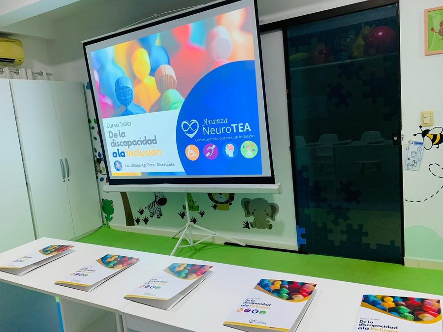 Sala preparada para el curso taller De la discapacidad a la inclusión, con el material impreso sobre las mesas y la presentación proyectada