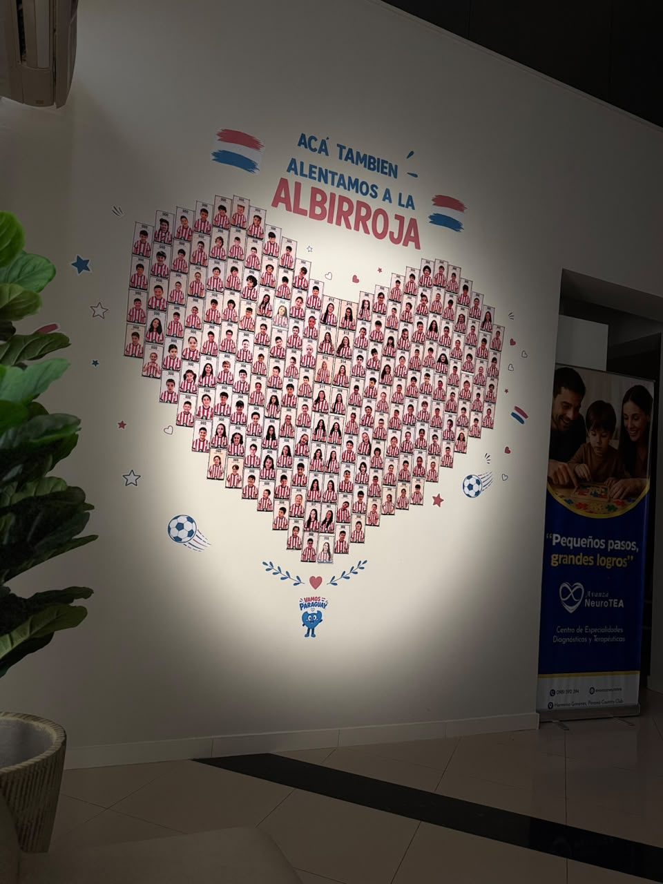 Mural con decenas de fotos de niños con la camiseta de Paraguay formando un corazón, y el texto: Acá también alentamos a la Albirroja