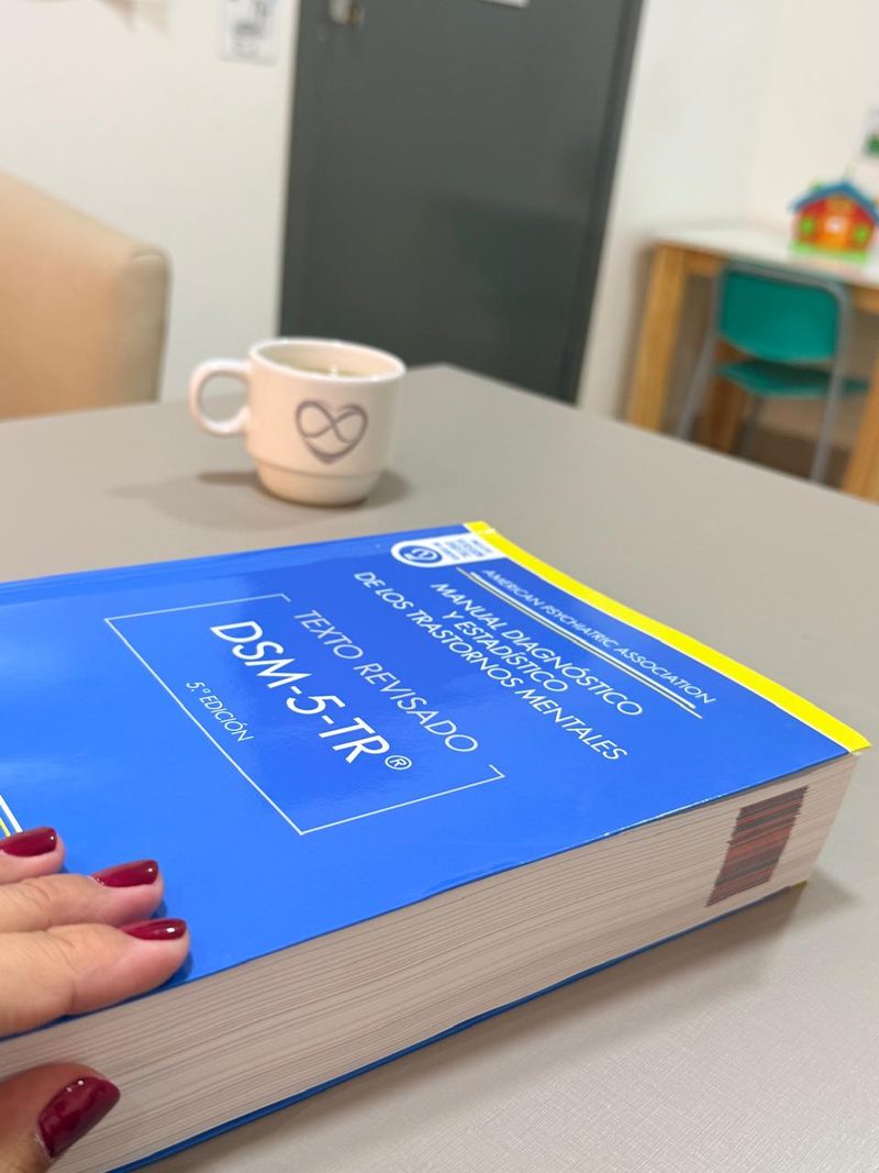 El manual diagnóstico DSM-5-TR sobre la mesa de un consultorio, junto a una taza con el logo de la clínica