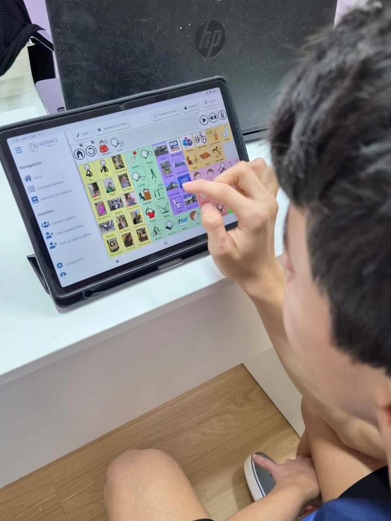 Un niño señala pictogramas en un tablero de comunicación aumentativa en una tableta, durante una sesión de fonoaudiología
