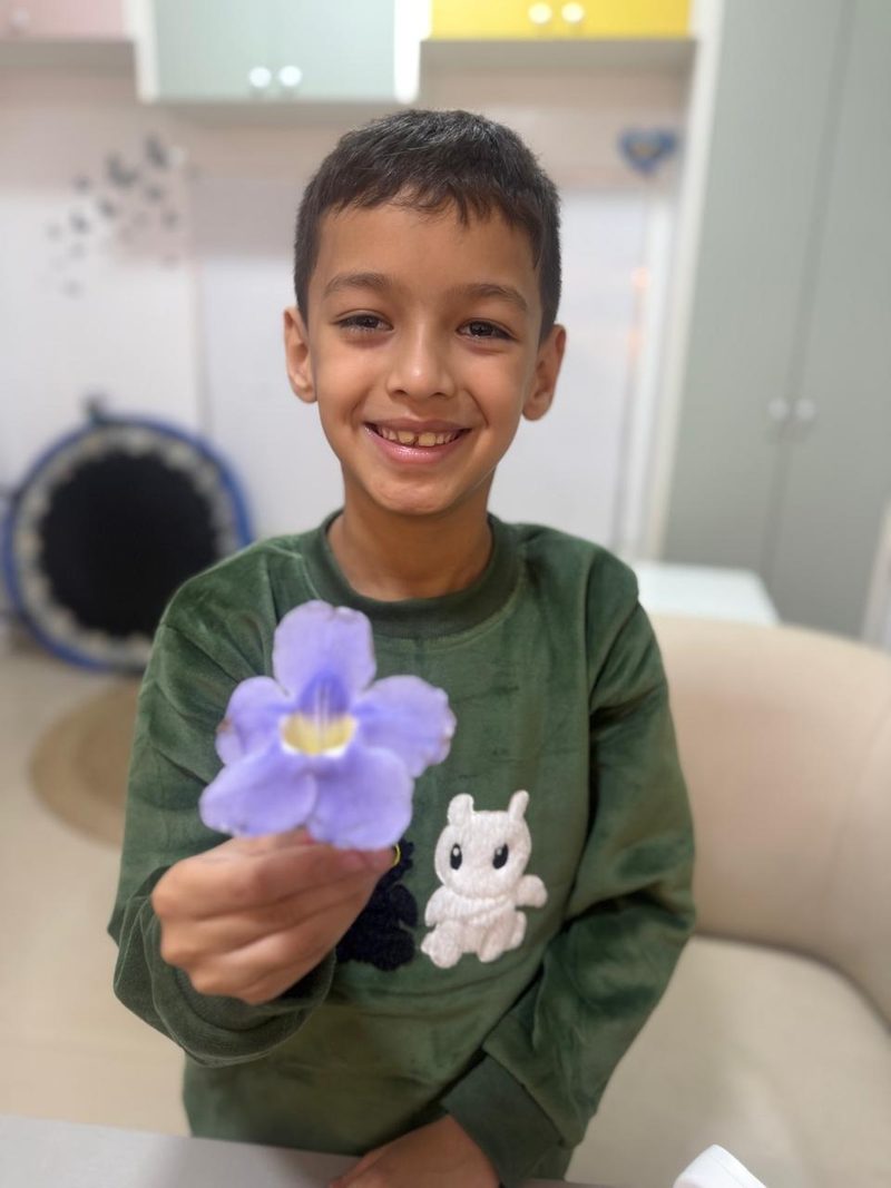 Un niño sonríe mostrando una flor violeta que sostiene en la mano, en el consultorio