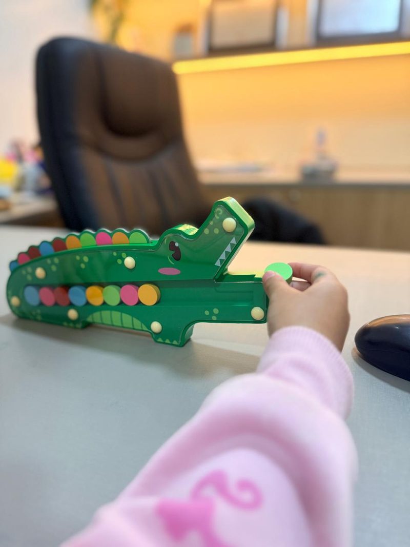 La mano de una niña coloca una ficha en un juego de cocodrilo de colores, trabajando turnos y espera