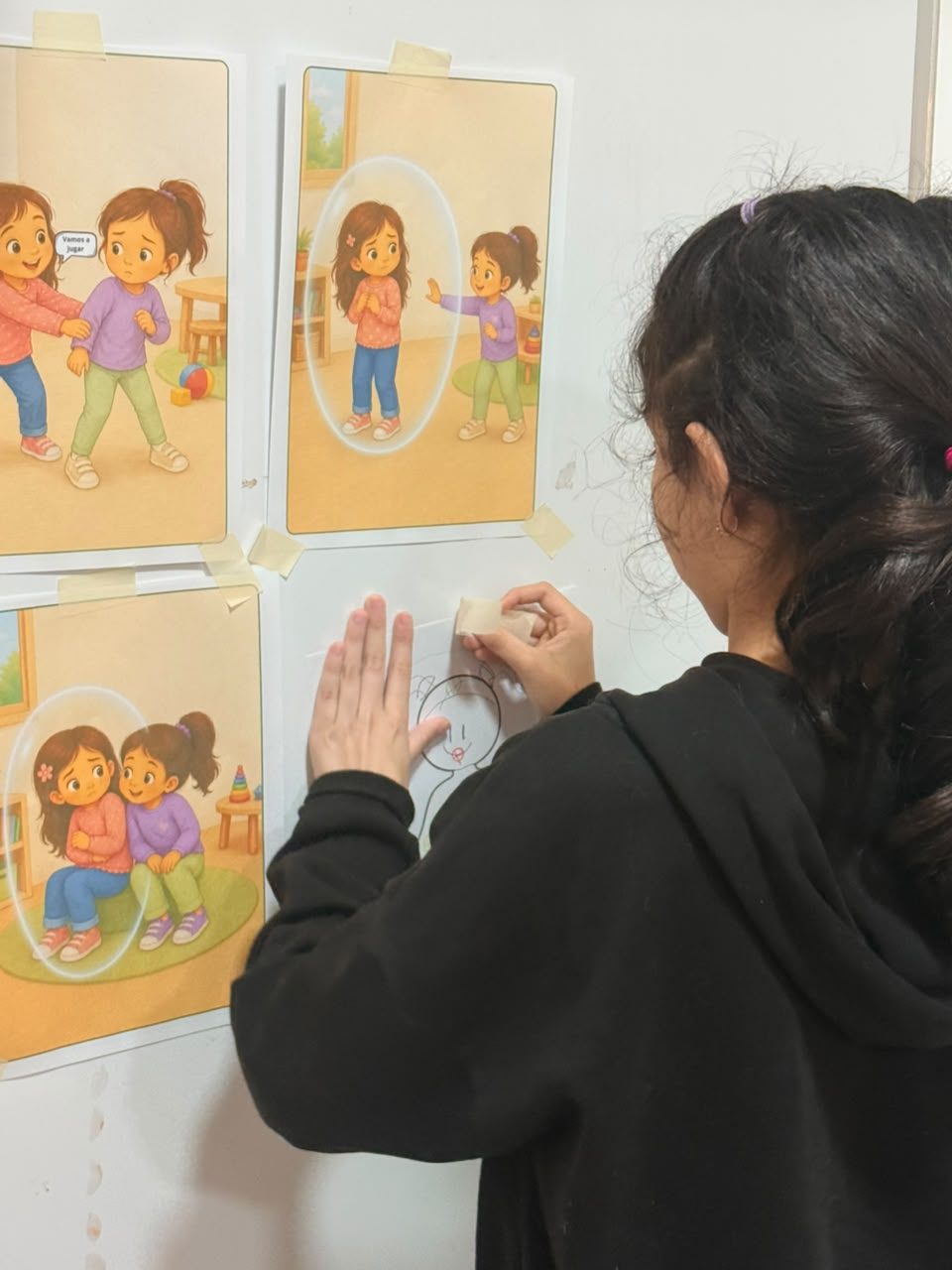 Una niña, de espaldas, pega láminas con pictogramas en la pared de la sala