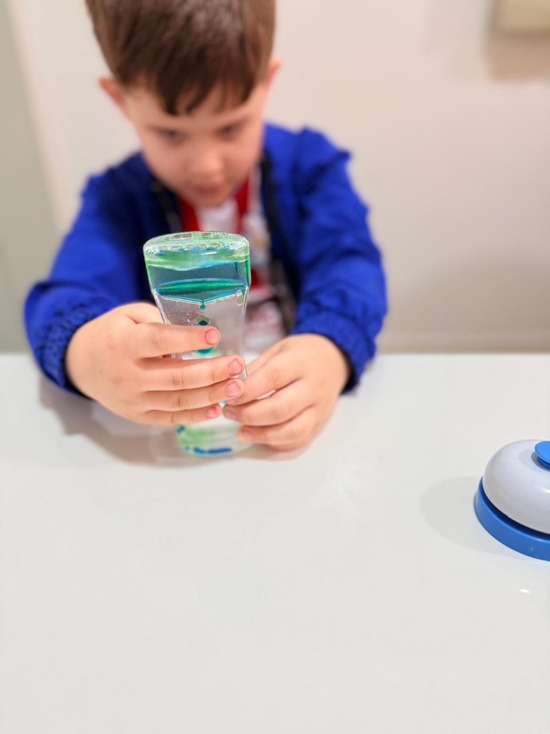 Un niño observa de cerca un reloj de líquido con burbujas de colores, un recurso de regulación sensorial